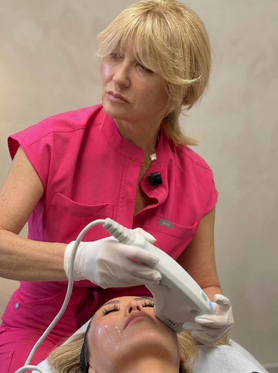Victoria Fedin in pink scrubs performing an Ultherapy treatment, guiding the transducer along a reclining patient's jawline